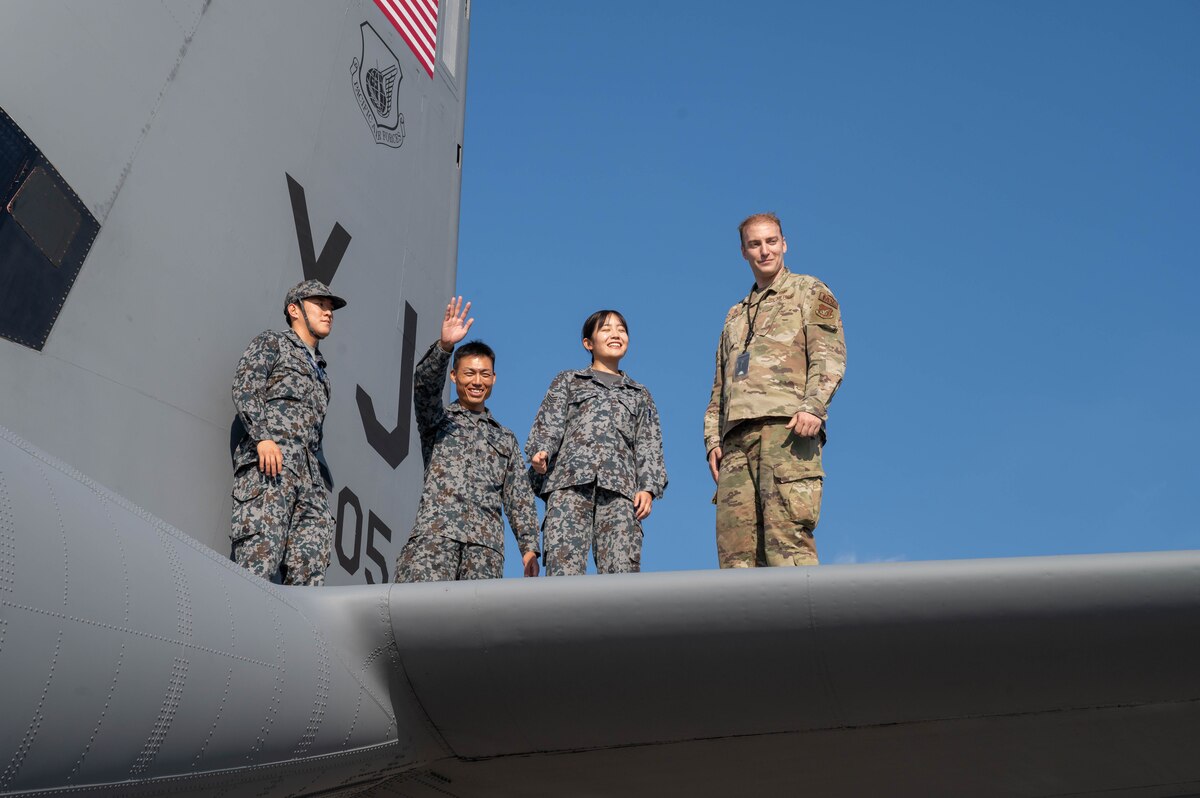 Four people in uniform are in the photo. They are posing for a photo while standing on the wing of an aircraft.