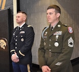 Army Officer and Enlisted Soldiers stand at parade rest.