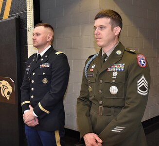 Army Officer and Enlisted Soldiers stand at parade rest.
