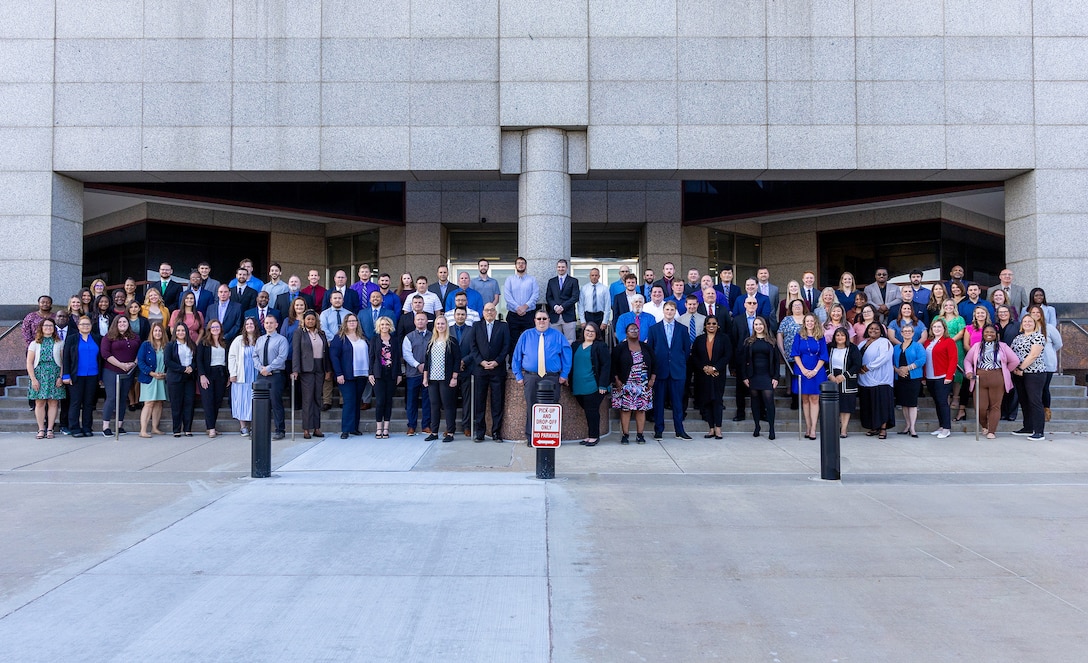 A group of smiling people stand outside on some steps.