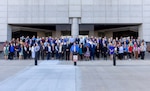 A group of smiling people stand outside on some steps.