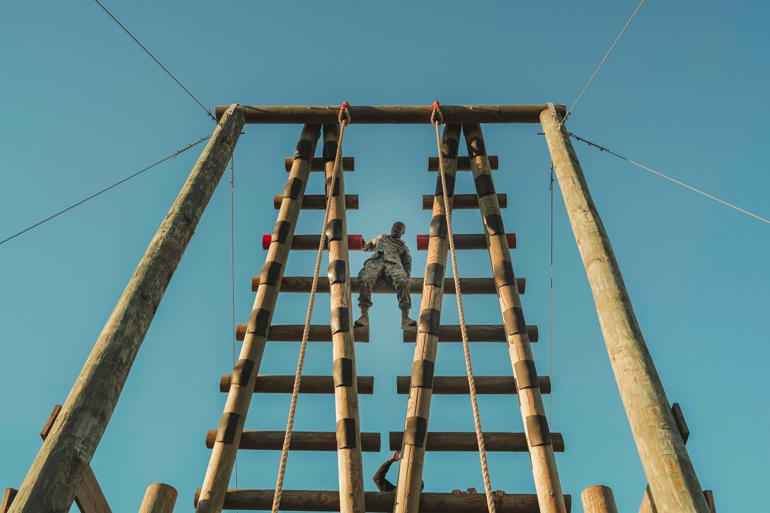 A Marine climbs a double wooden ladder as part of an obstacle course as seen from below.