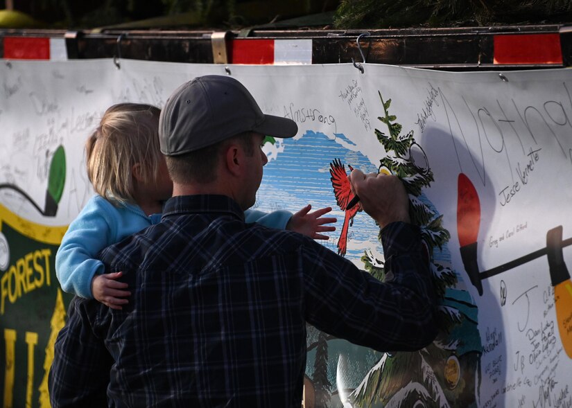 Attendees of the Capitol Christmas Tree event sign a banner on the truck carrying the Capitol Christmas Tree at Joint Base Andrews, Md., Nov. 16, 2023. During the event, service members and families viewed the Capitol Christmas Tree, signed the truck banner, and participated in arts and crafts. (U.S. Air Force photo by Senior Airman Austin Pate)