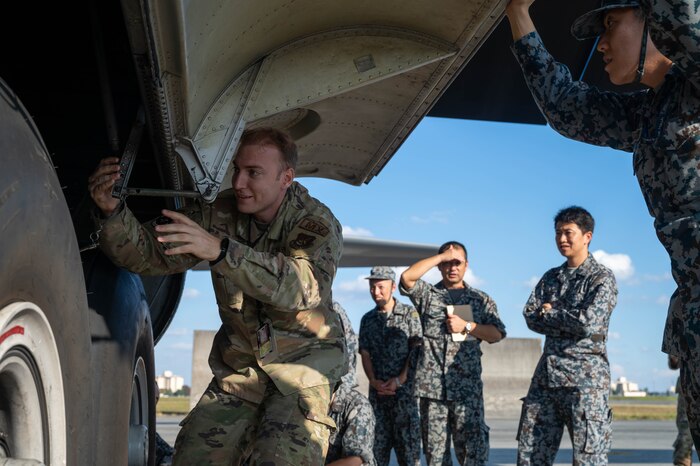 Six people in uniform are in the photo. One of them is interacting with the side of the aircraft while the other people are watching.