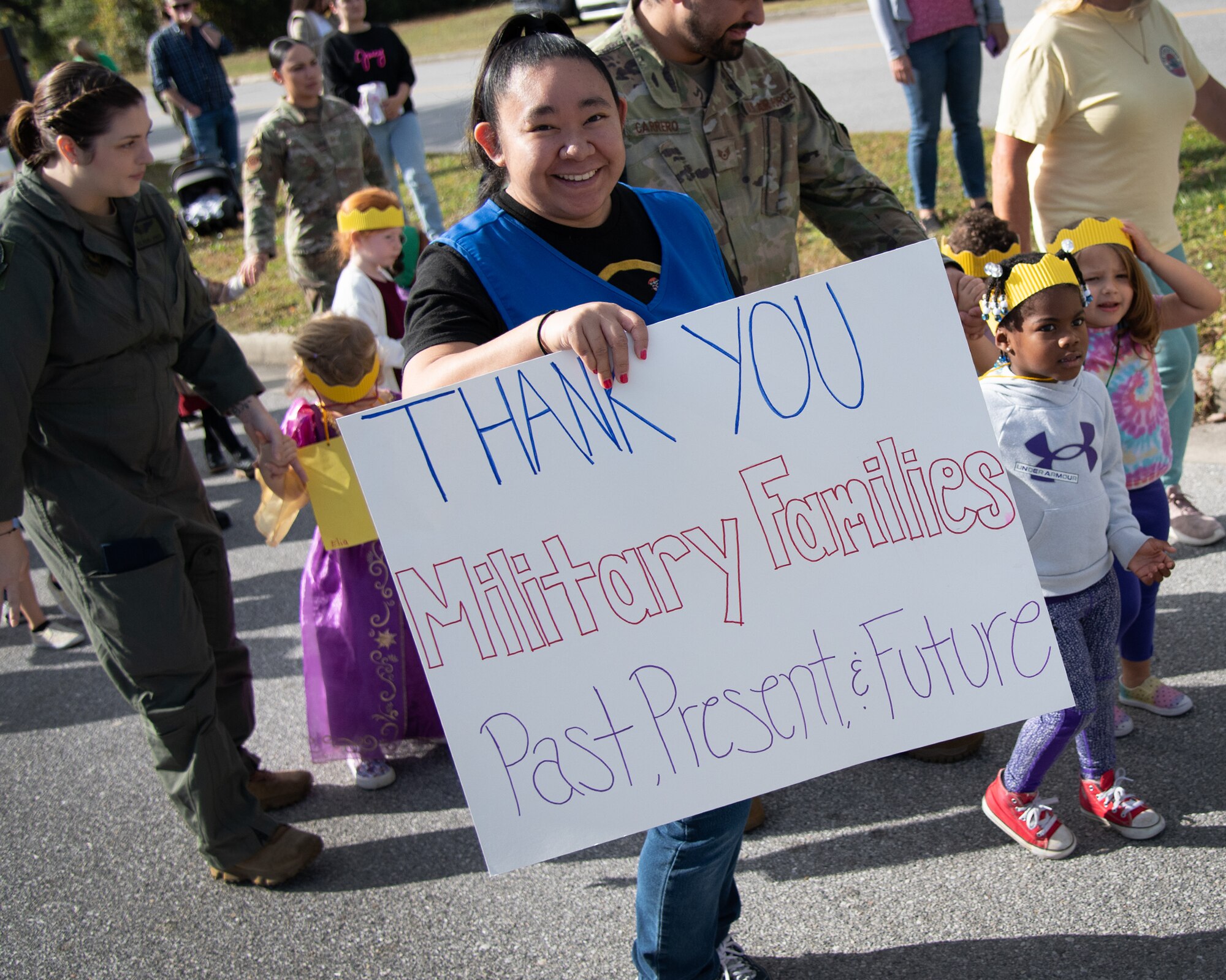A woman holds a sign in a parade with kids.