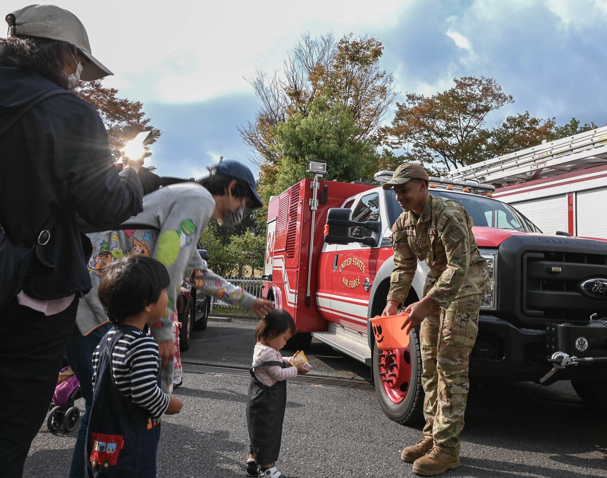 Man in uniform handouts out candy to a child with a fire truck parked behind him.