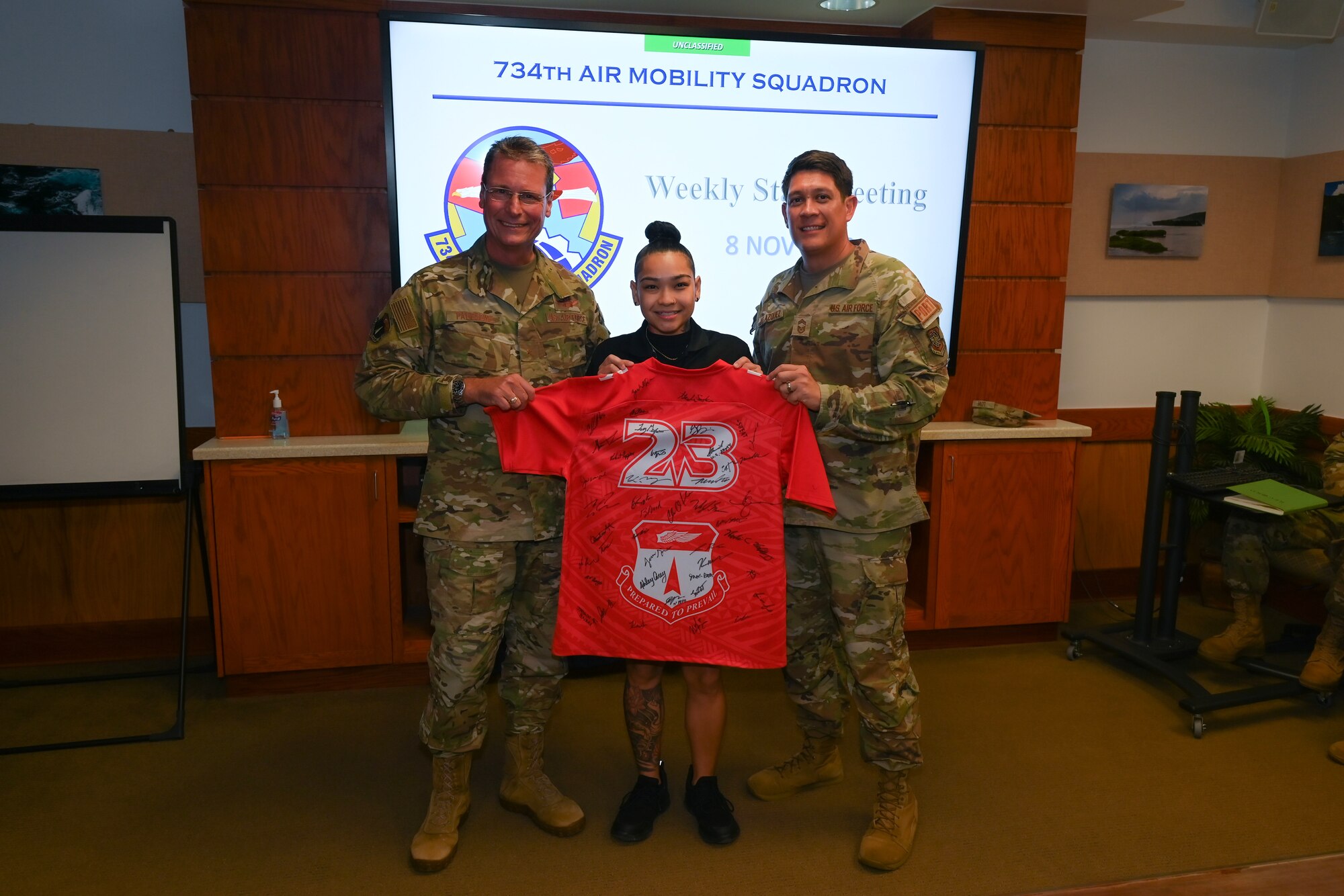 A government worker took a picture with two Airmen while holding a jersey.