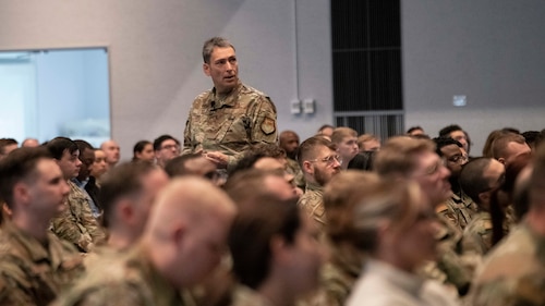 A military man stands in the middle of a seated audience.