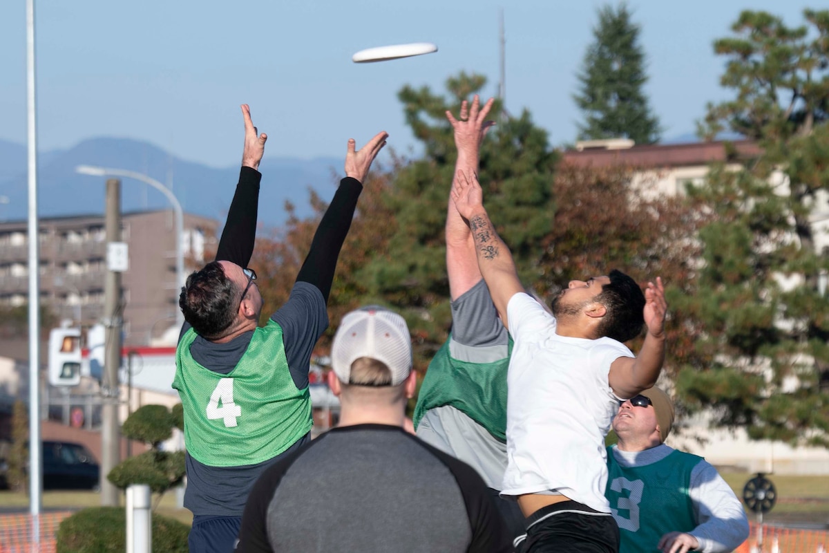 Military members reach for a frisbee.