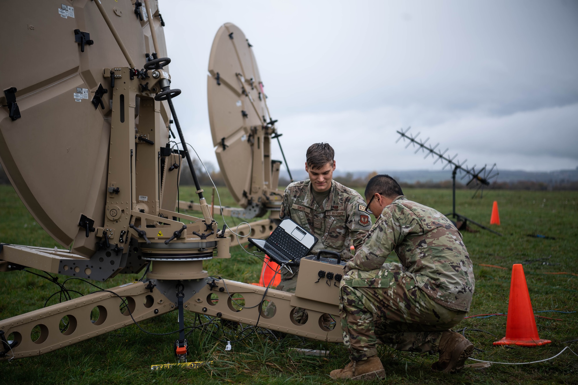 U.S. Air Force Airman 1st Class Ryan Smith, left, and Airman 1st Class Yekun Yang, right, 1st Combat Communications Squadron radio frequency transmissions system technicians, check cable connections on a satellite dish during exercise HEAVY RAIN 23, at Grostenquin, France, Nov. 16, 2023. HEAVY RAIN is a U.S. Air Forces in Europe-led command and control exercise that integrates communicators, operators and aggressors from joint forces, NATO allies and partners, testing and evaluating their communication and data-sharing capabilities in a rapidly changing operating environment. (U.S. Air Force photo by Senior Airman Jared Lovett)