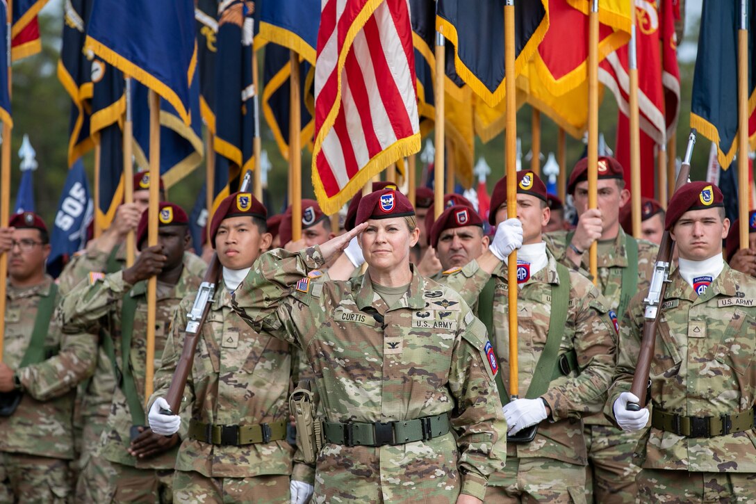 Soldiers salute and hold flags above their heads while standing at attention during a ceremony.