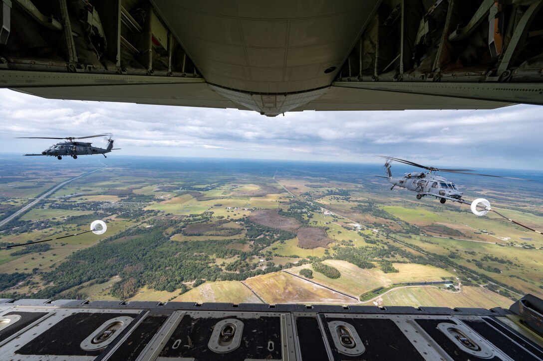 Two helicopters fly behind a large aircraft during an aerial refueling.