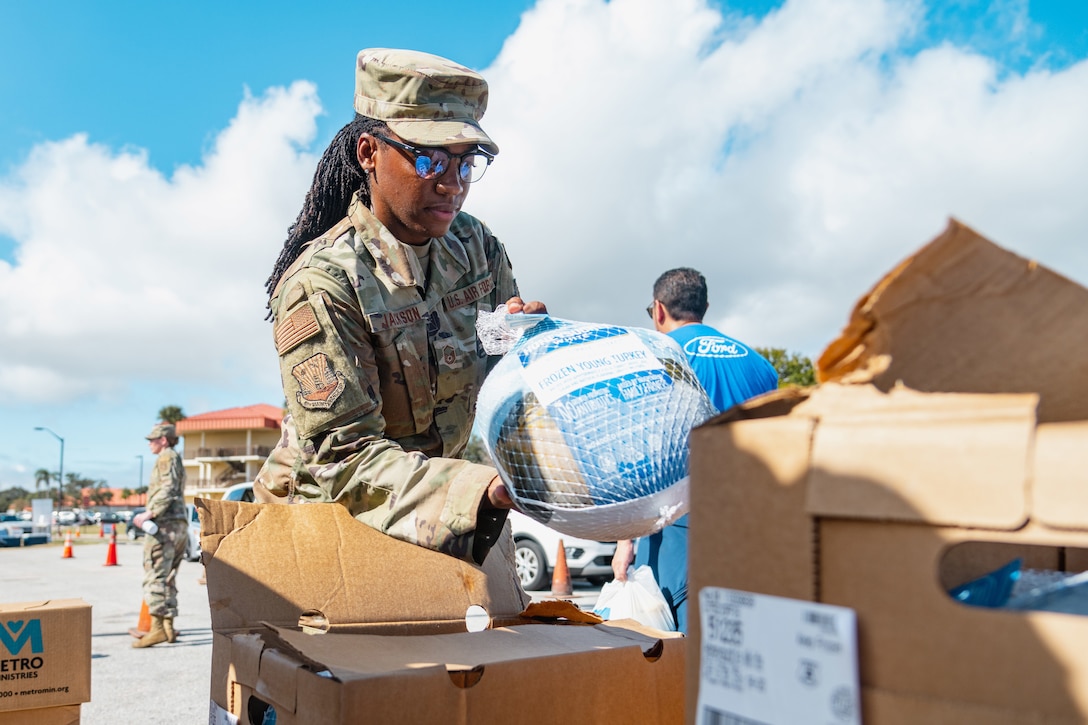An airman takes a packaged turkey out of a cardboard box.