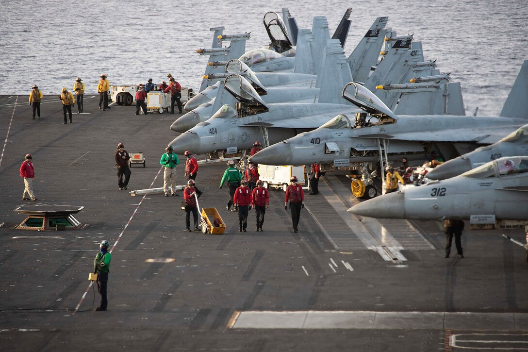 Sailors prepare F/A-18 Super Hornets for flight operations on the deck of an aircraft carrier.