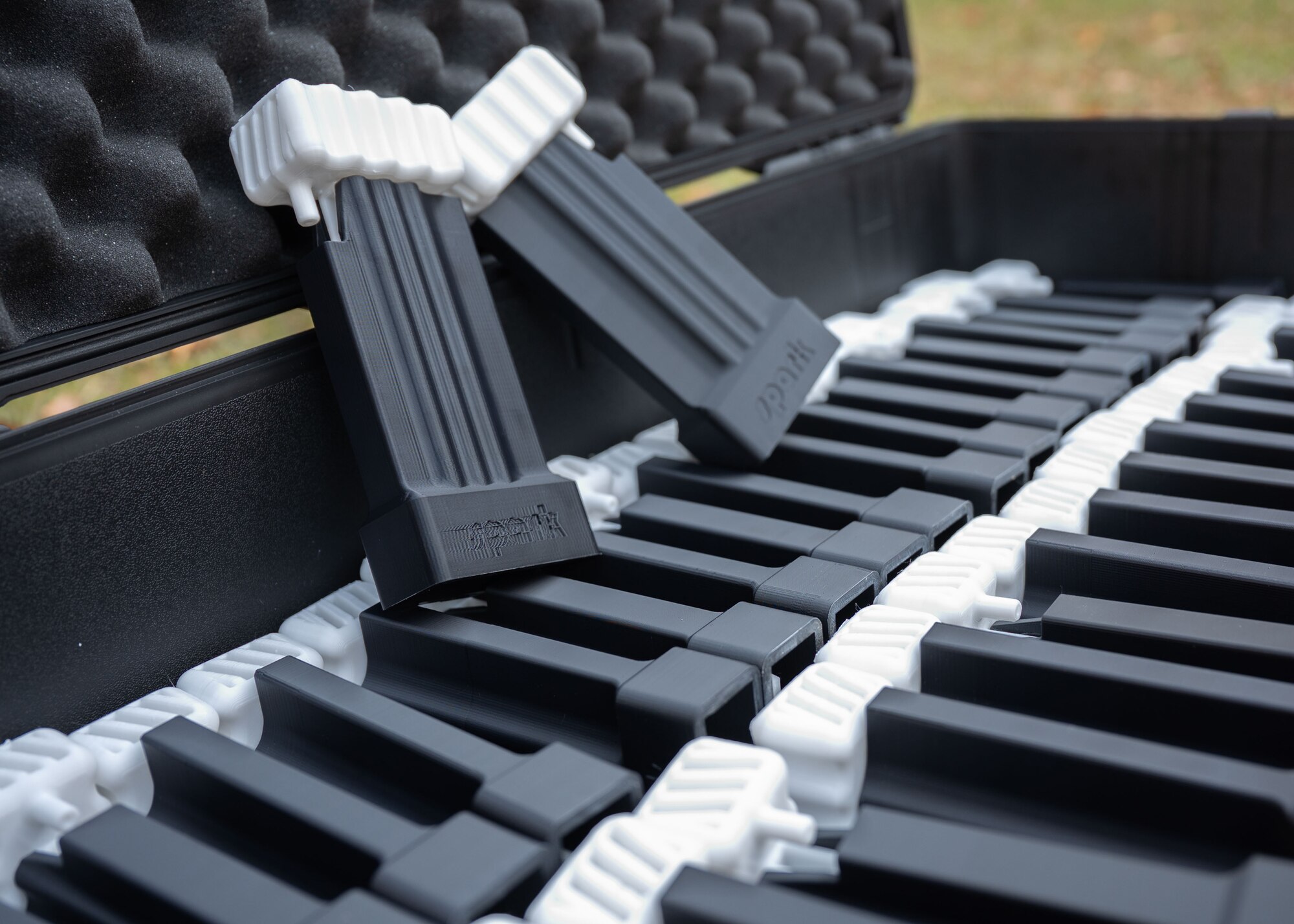 Two 3-D printed magazine loaders sit on top of an opened case filled with additional 3-D printed magazine loaders.