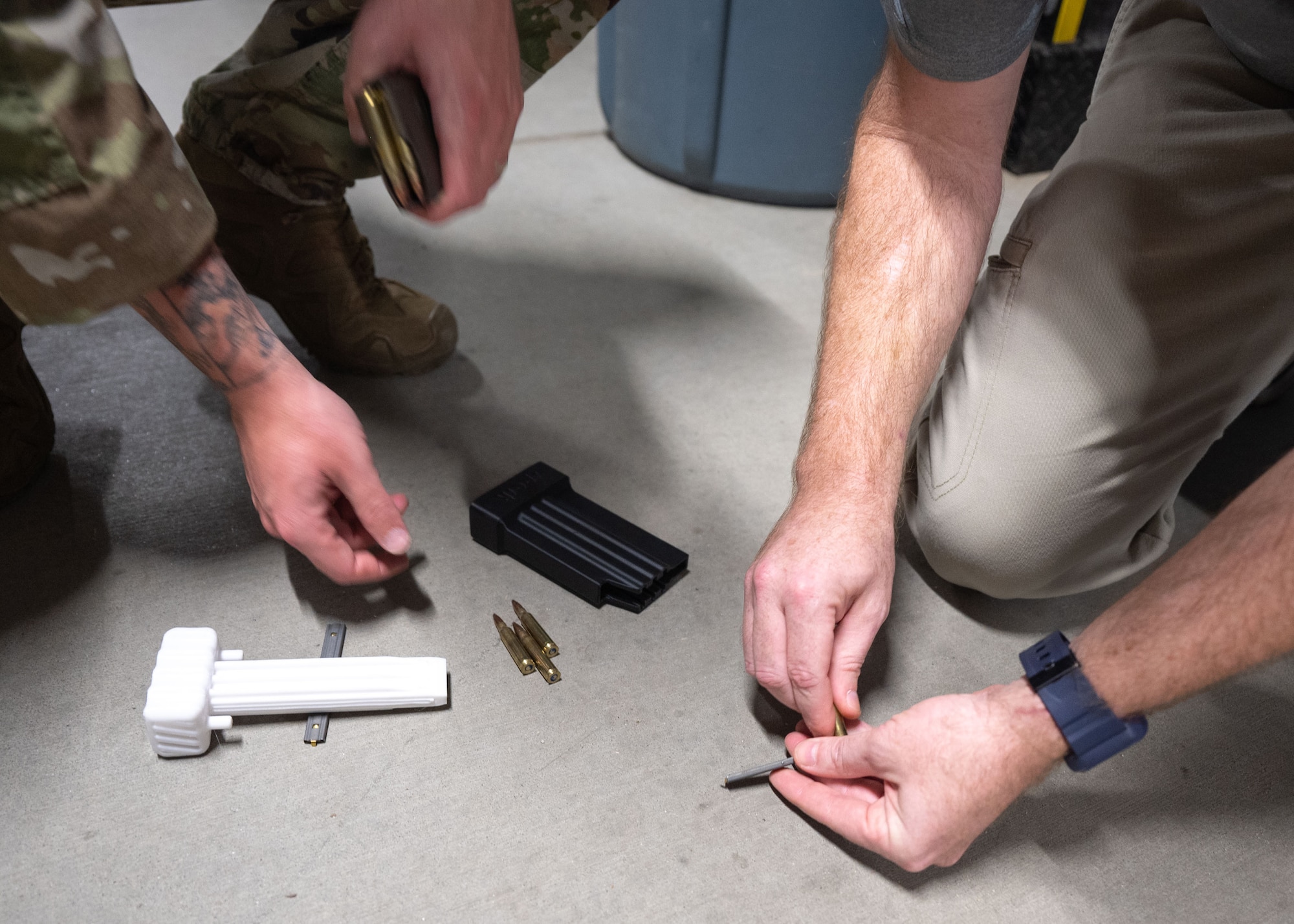 A close up of two sets of hands loading individual rounds of ammunition off the ground into a magazine.