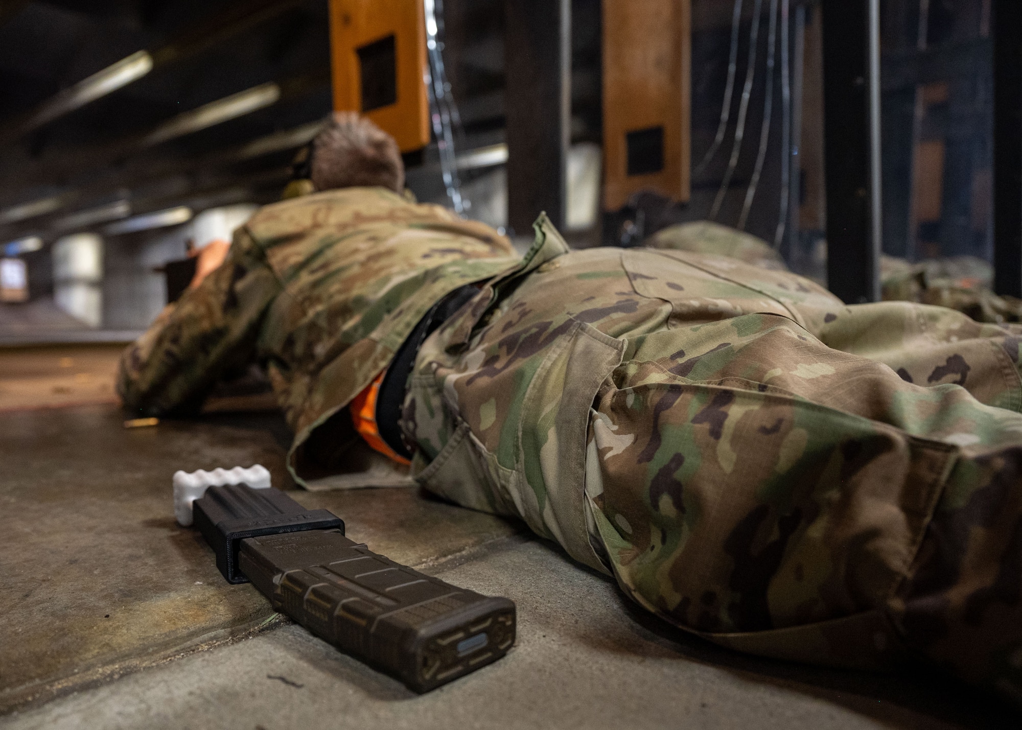 Side view of a man laying down firing at a shooting range with a 3-D printed loading magazine attached to an M-4 carbine magazine.