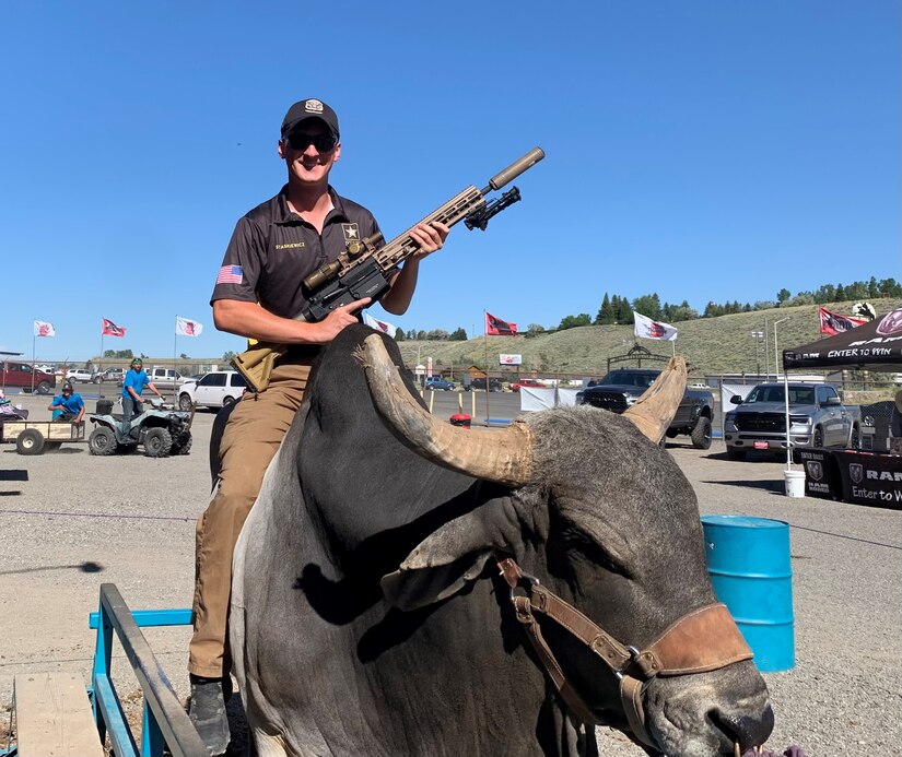 Man in Army Polo holding a gun while sitting on a live bull.