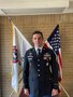 Man in Army uniform poses in front of the American flag and USAREC flag.