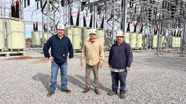 Three men standing outside of hydropower plant by electrical wirings.