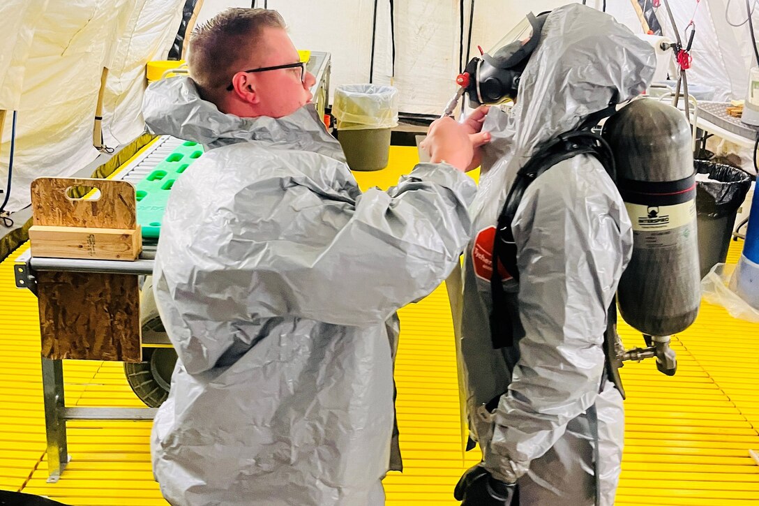A soldier fixes another person’s protective suit during training.