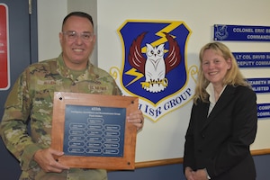 Lt. Col. Brent Allen (left), director of the Joint Regional Intelligence Center at the National Air and Space Intelligence Center (NASIC) and retired Lt. Col. Audrey Swinney, NASIC customer engagement and protocol, stand with the 655th Intelligence, Surveillance and Reconnaissance (ISR) Group Proffer Tray that identifies the group’s original 16 plank holders. They along with another 655th ISRG plank holder were honored with planks on Nov. 3, 2023, at the 655th ISR Wing headquarters.