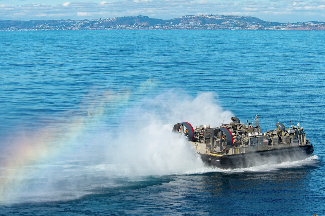A boat sails to the right as a rainbow appears to the left with mountains in the background.