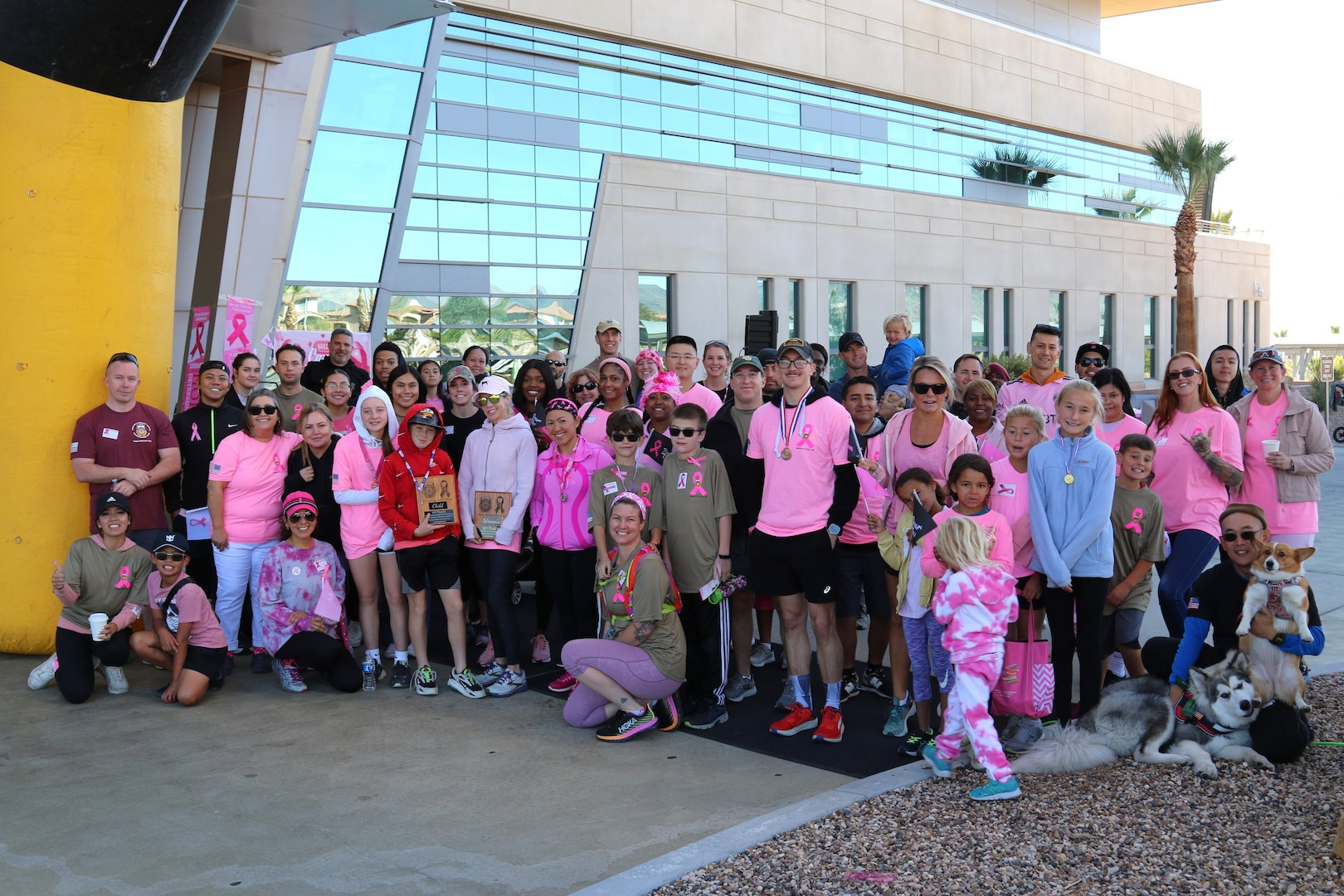 Group of 50 people posing for picture while wearing various pink attire to commemorate breast cancer awareness month.