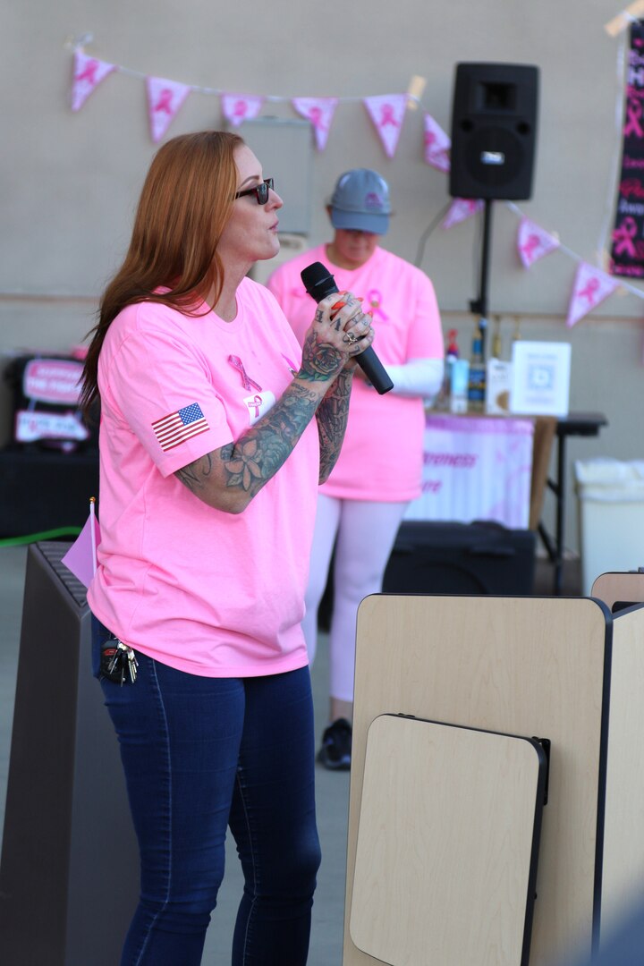 Woman wearing pink talks to crowd on a microphone.