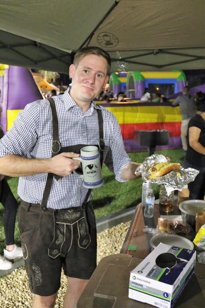 Person holding beer stein dressed in German attire holding a hot dog.