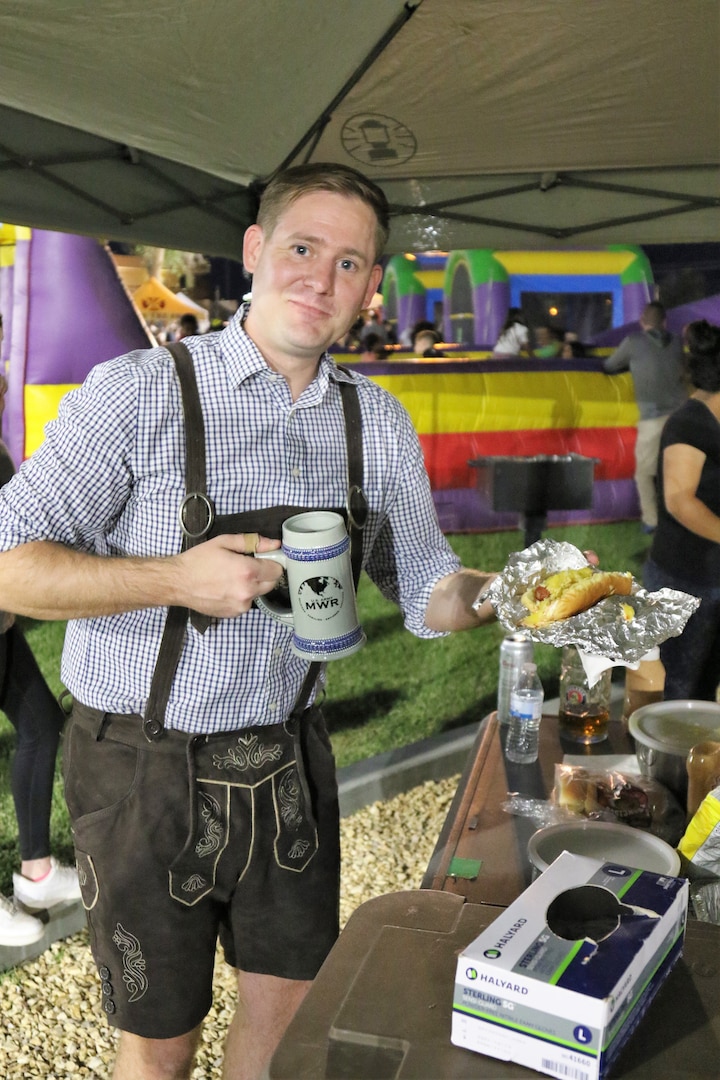 Person holding beer stein dressed in German attire holding a hot dog.