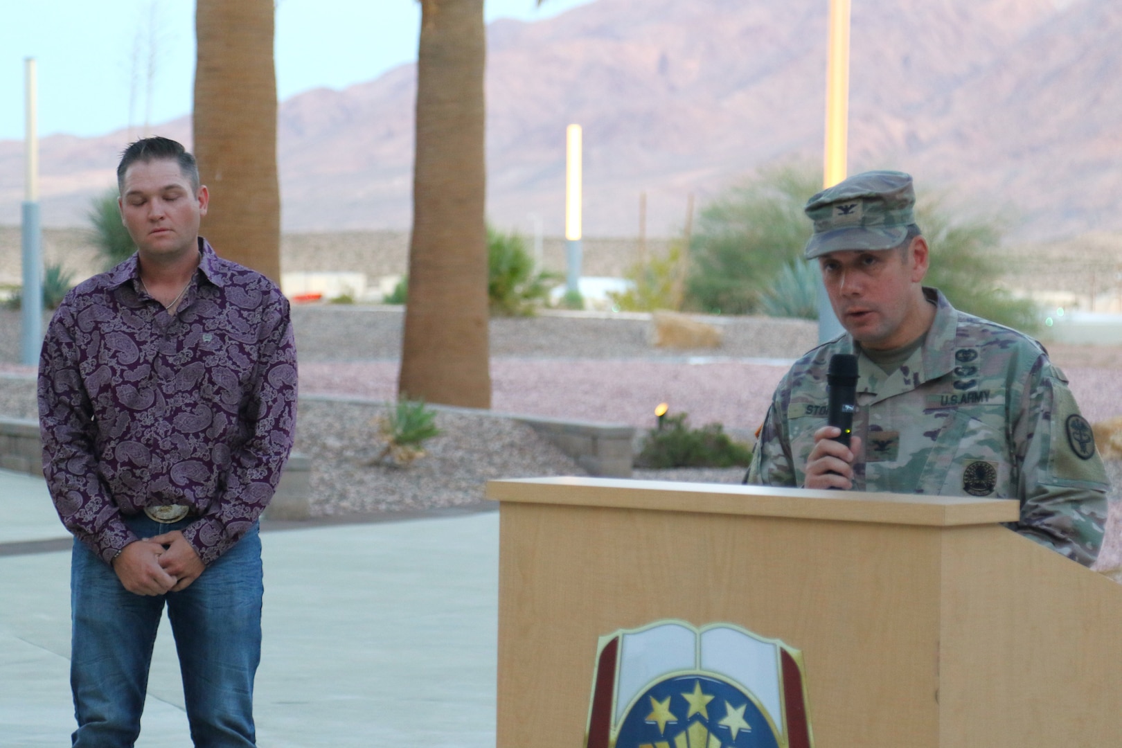 Military commander giving a speech while a somber host stands nearby.