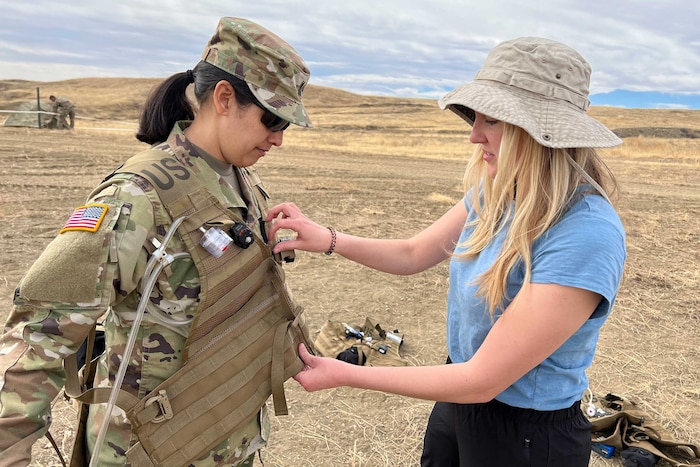 A scientist puts a vest on a soldier.