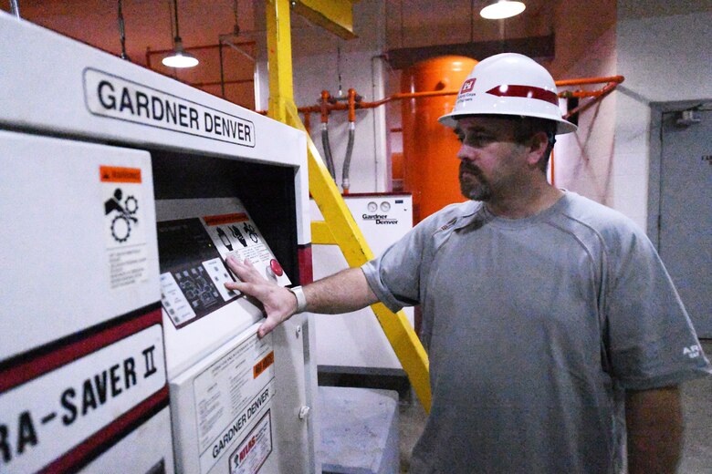 Man wearing hardhat looks at hydropower control panel.