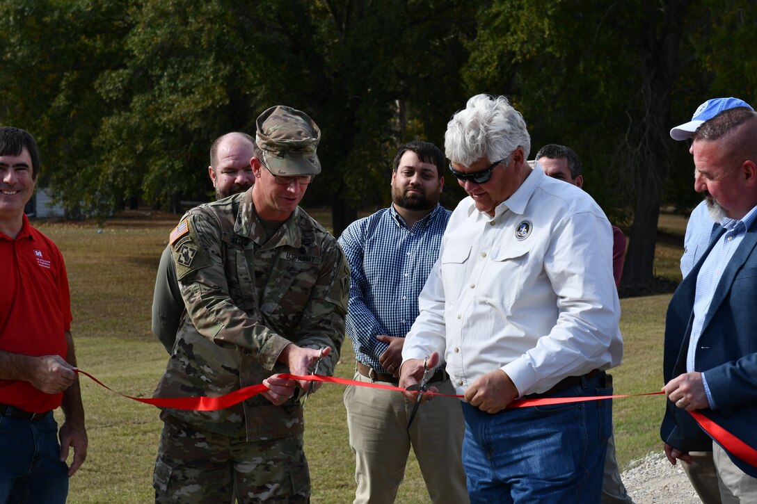 A man in a U.S. Army Colonel's uniform and a man in business casual clothes cut a ceremonial red ribbon.