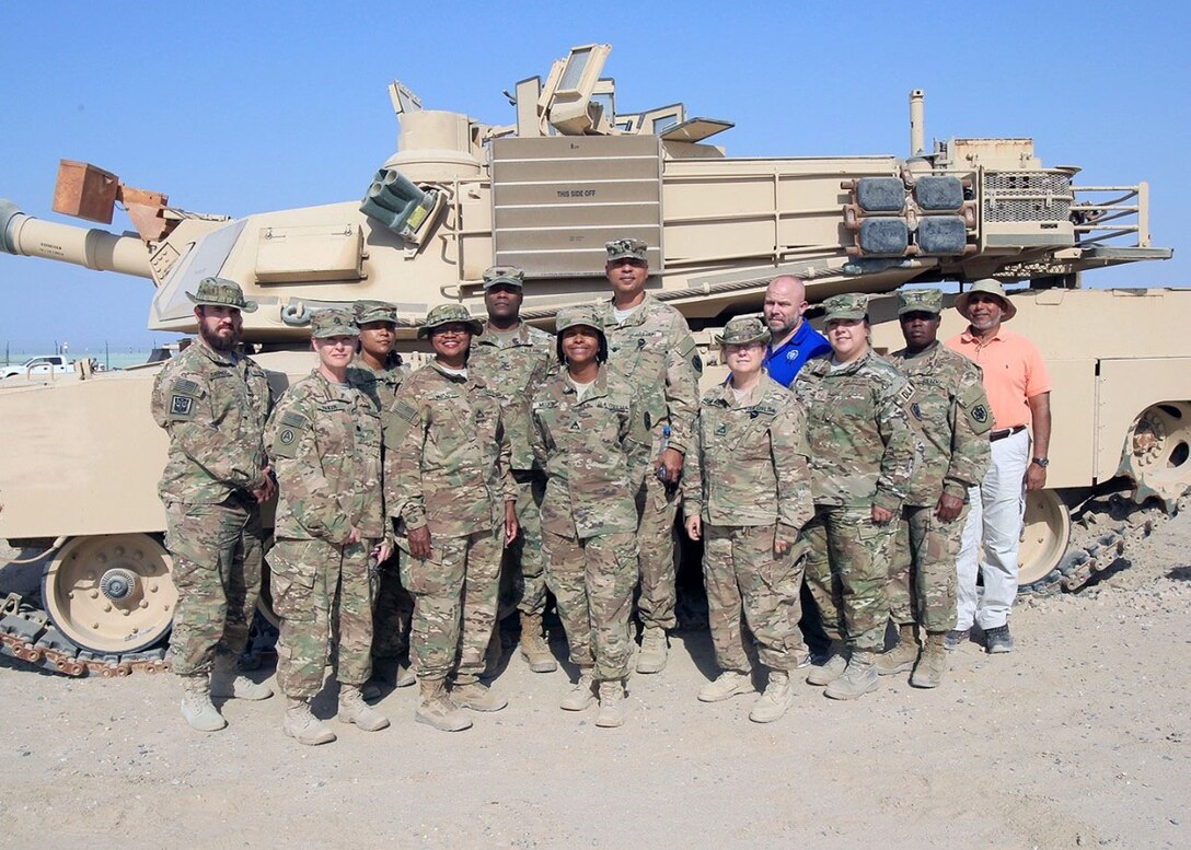 Group stands in front of military vehicle.