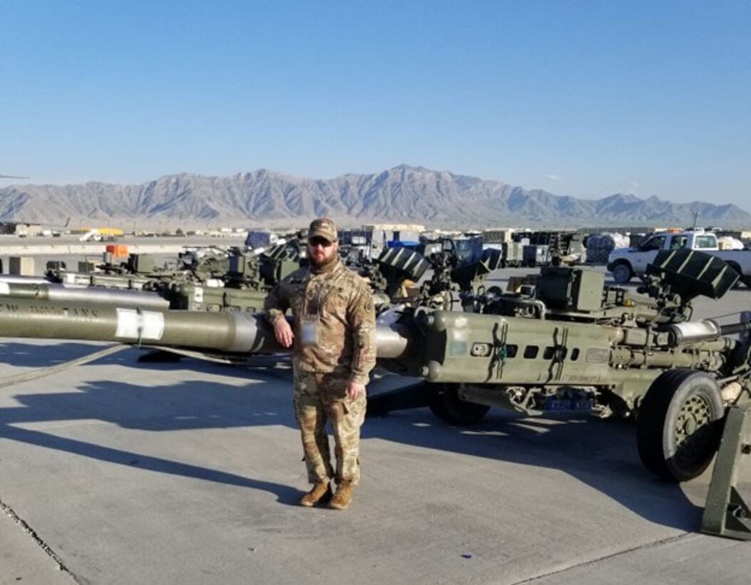 Man in military gear standing in front of M777 howitzer.