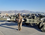 Man in military gear standing in front of M777 howitzer.