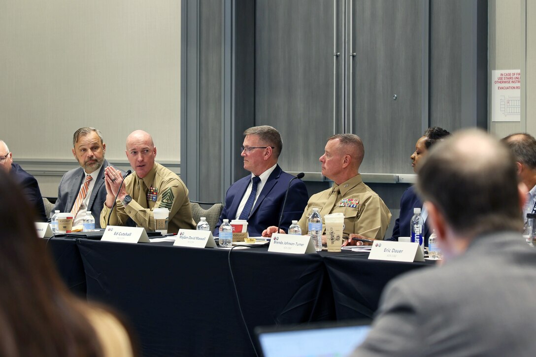 A group of men in suits and Marine Corps uniforms talking at a conference table.