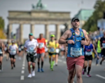 Chris Allen, in focus in the foreground wearing running gear and a racing number, with other runners and Berlin landmarks in the background