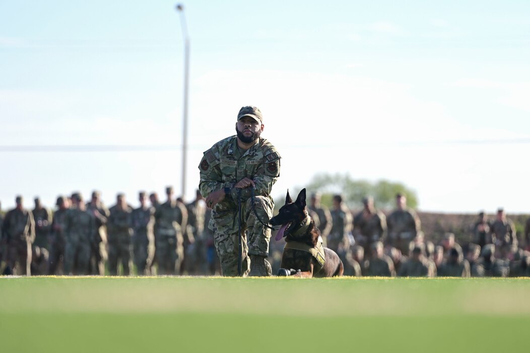 U.S. Air Force Staff Sgt. Keith Ferguson, 17th Security Forces Squadron military working dog handler, sits with MWD Borys, 17th SFS detection dog, during the 17th Training Wing Drill Down Competition at Mathis Field, Goodfellow Air Force Base, Texas, Nov. 17, 2023. Before the drill down exhibition began, the 17th SFS put on a short MWD demonstration to show students MWD’s training on a daily basis and exhibited a practical exercise with simulated scenarios. (U.S. Air Force photo by Airman 1st Class Madison Collier)