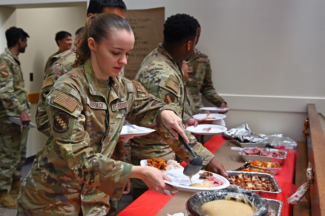 A uniformed service member prepares a plate of food next to several other uniformed service members.