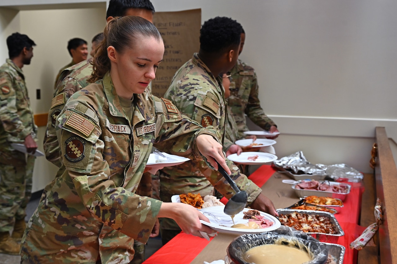 A uniformed service member prepares a plate of food next to several other uniformed service members.