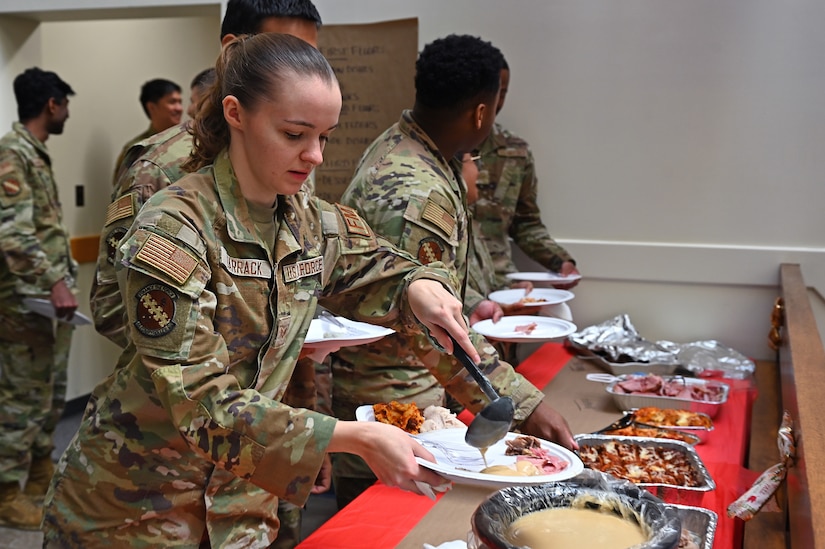 A uniformed service member prepares a plate of food next to several other uniformed service members.