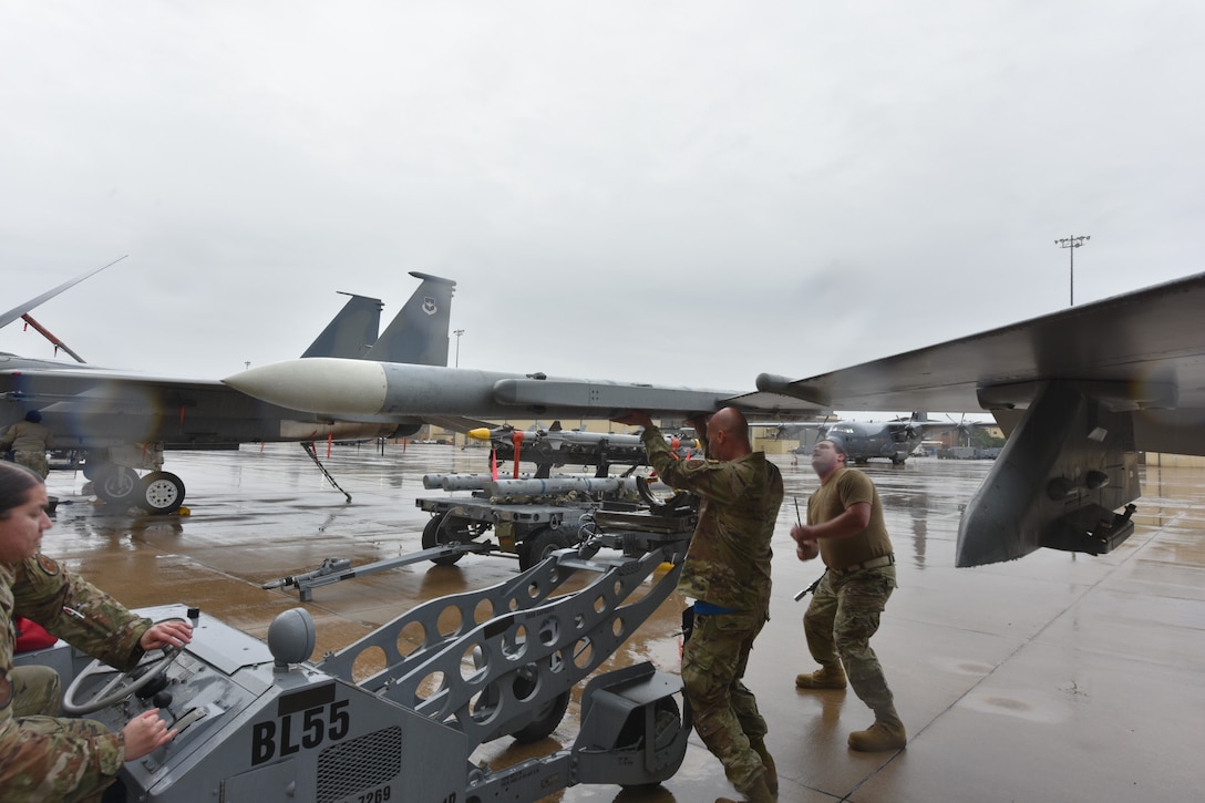 Three Airman load a bomb onto an aircraft