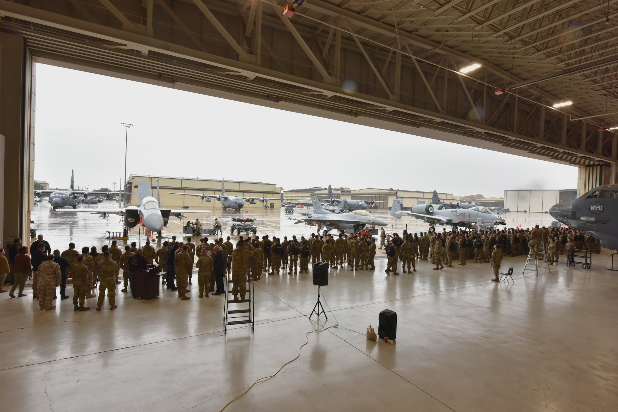 Airman stand in a hangar. Jets are outside the hangar.