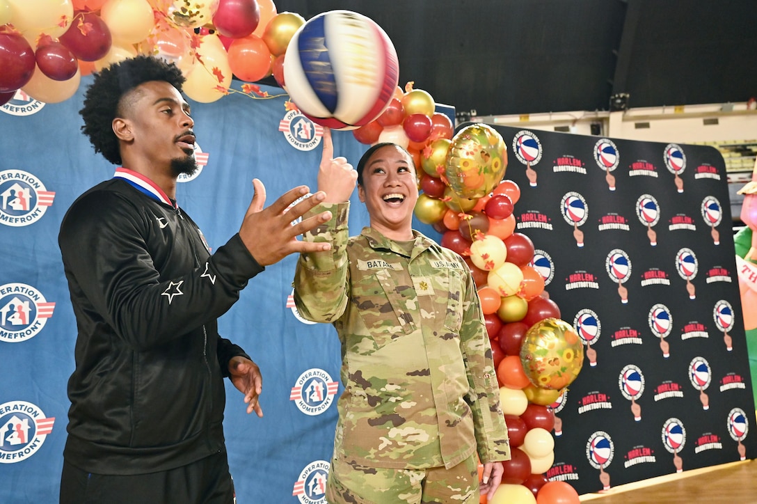 A basketball player watches as a soldier spins a basketball on their finger.