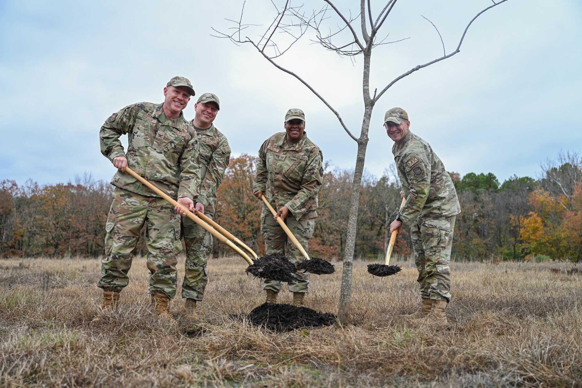 People in uniform hold shovels filled with dirt.