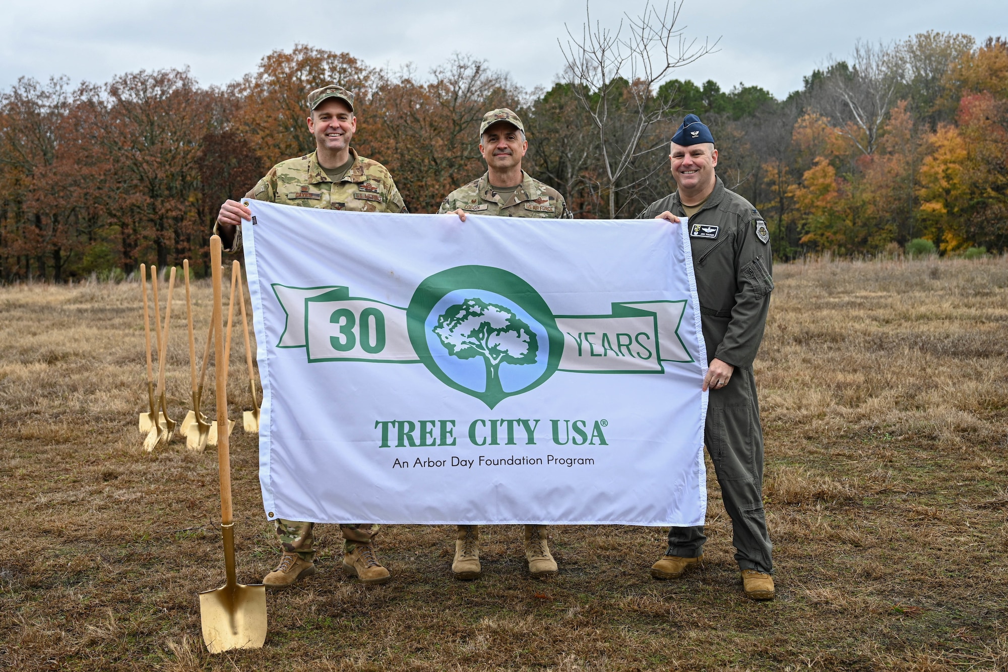 Three men in uniform hold a "tree city USA" flag.