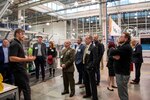 People gather to listen to a speaker on a factory floor.
